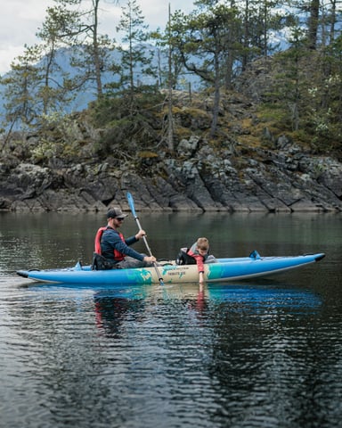 Two kayakers paddling near a forested rocky island on a calm lake