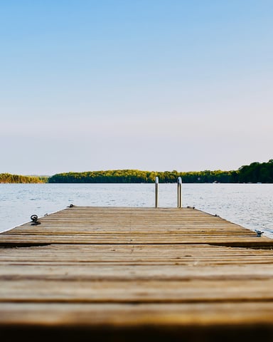 Wooden dock stretching out over a calm lake with forested hills in the distance