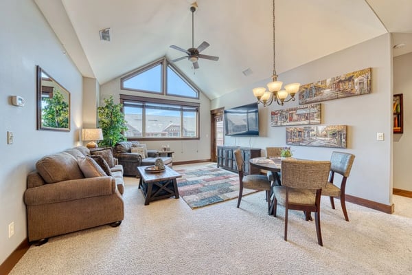 Red cottage with multi-level wooden deck, patio chairs, and fenced yard with mature trees