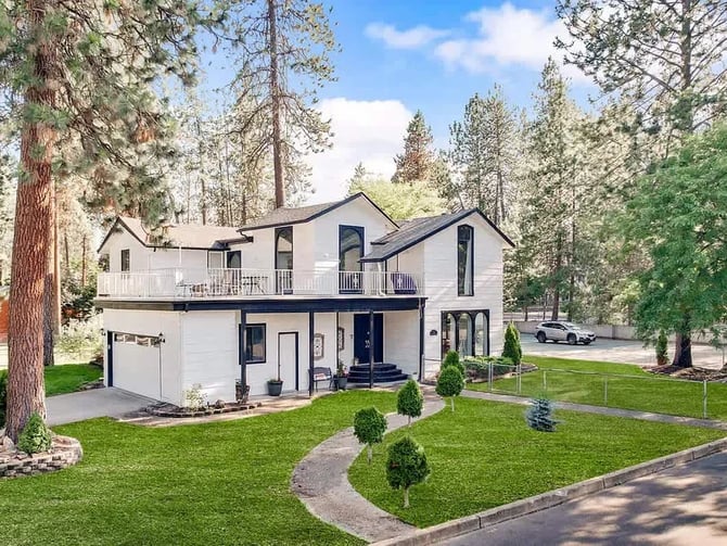 Exterior of the Movie Theater Retreat With Pickleball Court, a white two-story home among pine trees in Post Falls